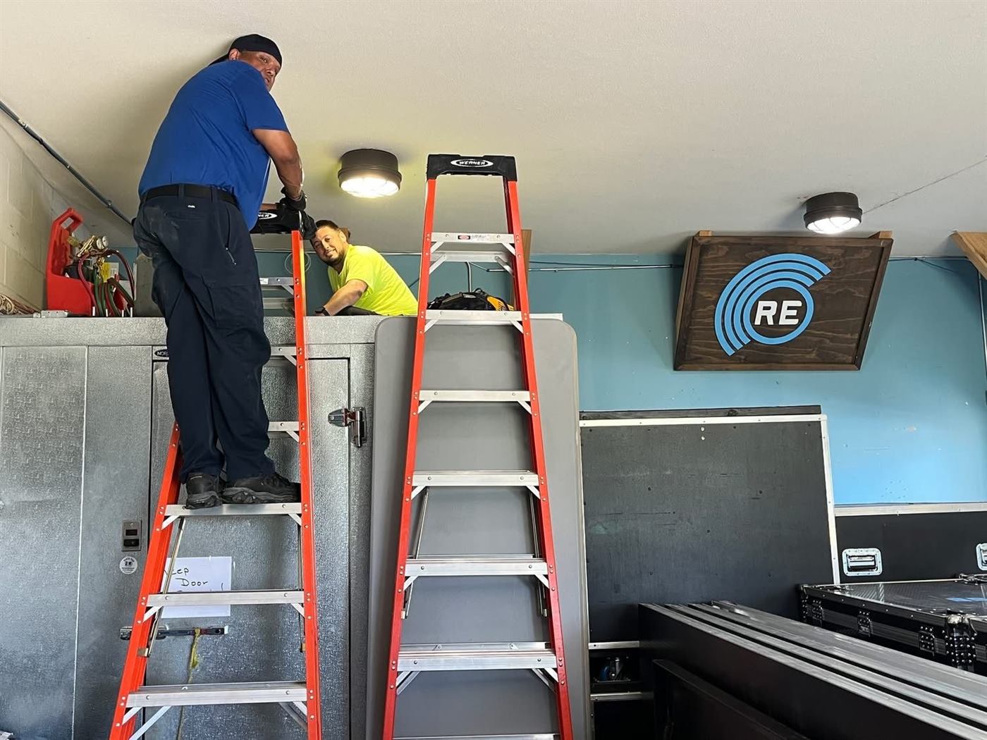 Technician on a ladder repairing equipment in a commercial space